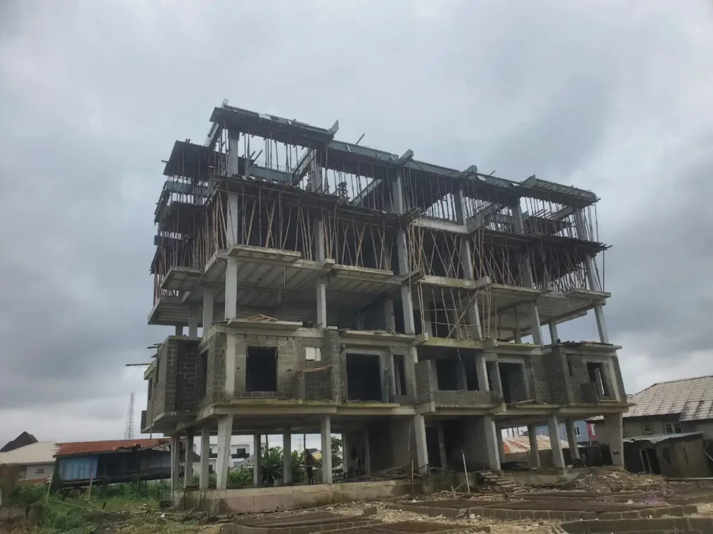 Redemption Tower Gbagada | Luxury 3-Bedroom Homes 2 Redemption Tower Gbagada under construction showing multi-storey reinforced concrete frame, blockwork, wooden formwork, and open floor plates against a cloudy sky